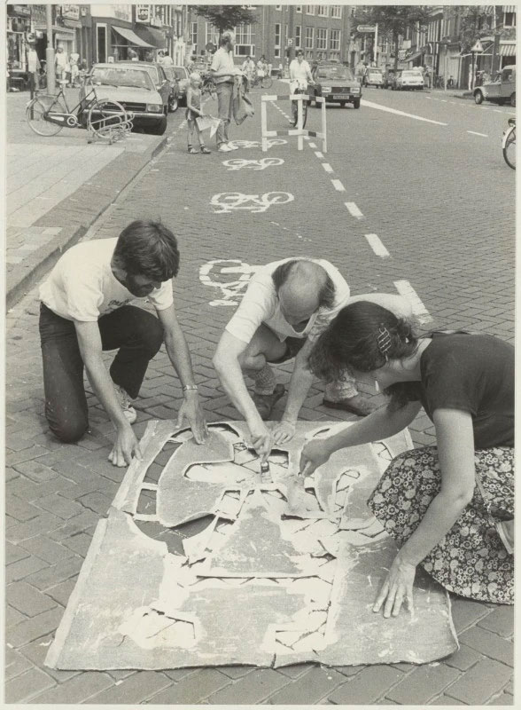 Membros da Cyclist's Union em ação na Gedempte Oude Gracht, usando stênceis para marcar uma ciclofaixa. Foto feita entre 1984 e 1986. Imagem via Wikimedia Commons – Noord-Hollands Archief / Fotoburo de Boer